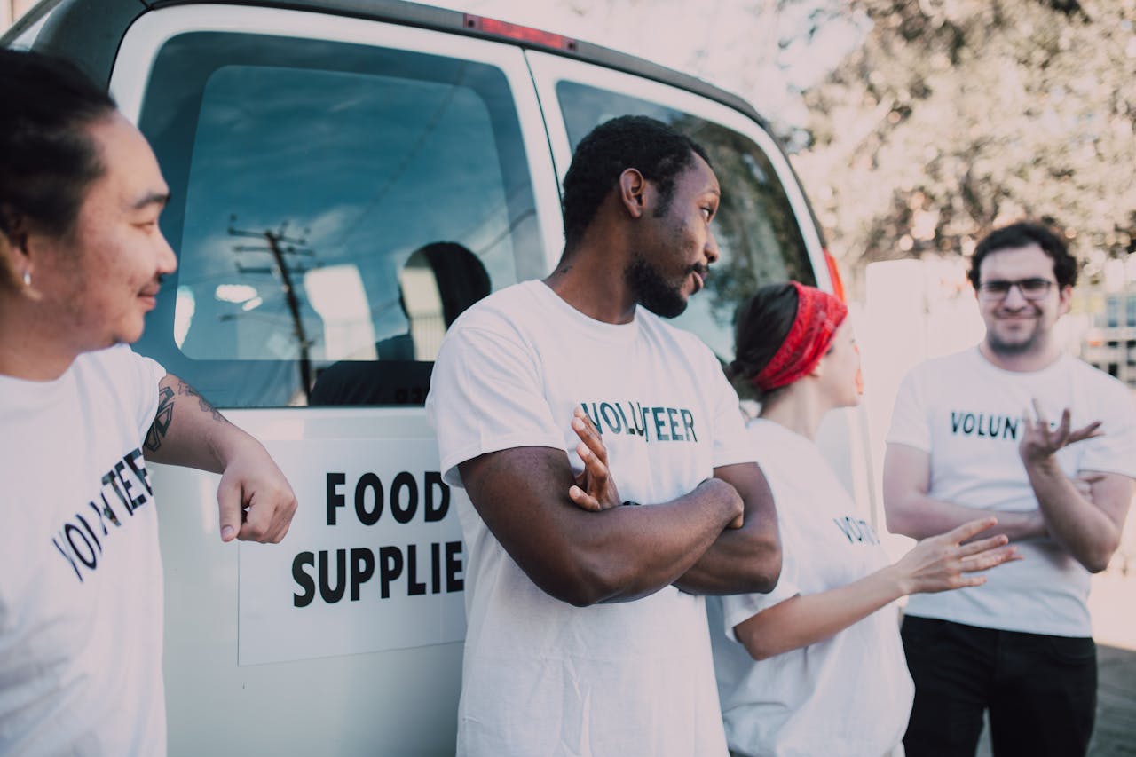 services-01 Volunteers gather beside a van to prepare and distribute food supplies outdoors.